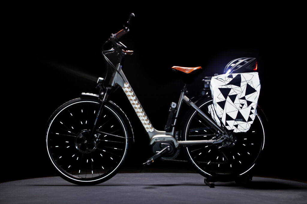 Una bicicletta elettrica color argento con borse posteriori ad alta visibilità, clip per raggi e un disegno riflettente sul telaio