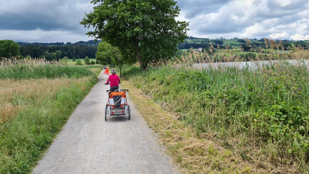 Familienvelotour Sempachersee Kanton Luzern: Velo mit Anhänger und Kind fährt dem Uferweg des Sempachersees entlang.
