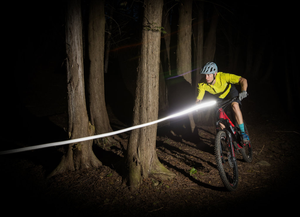 Biker de montagne se promenant dans les bois la nuit avec une forte lumière de bicyclette.