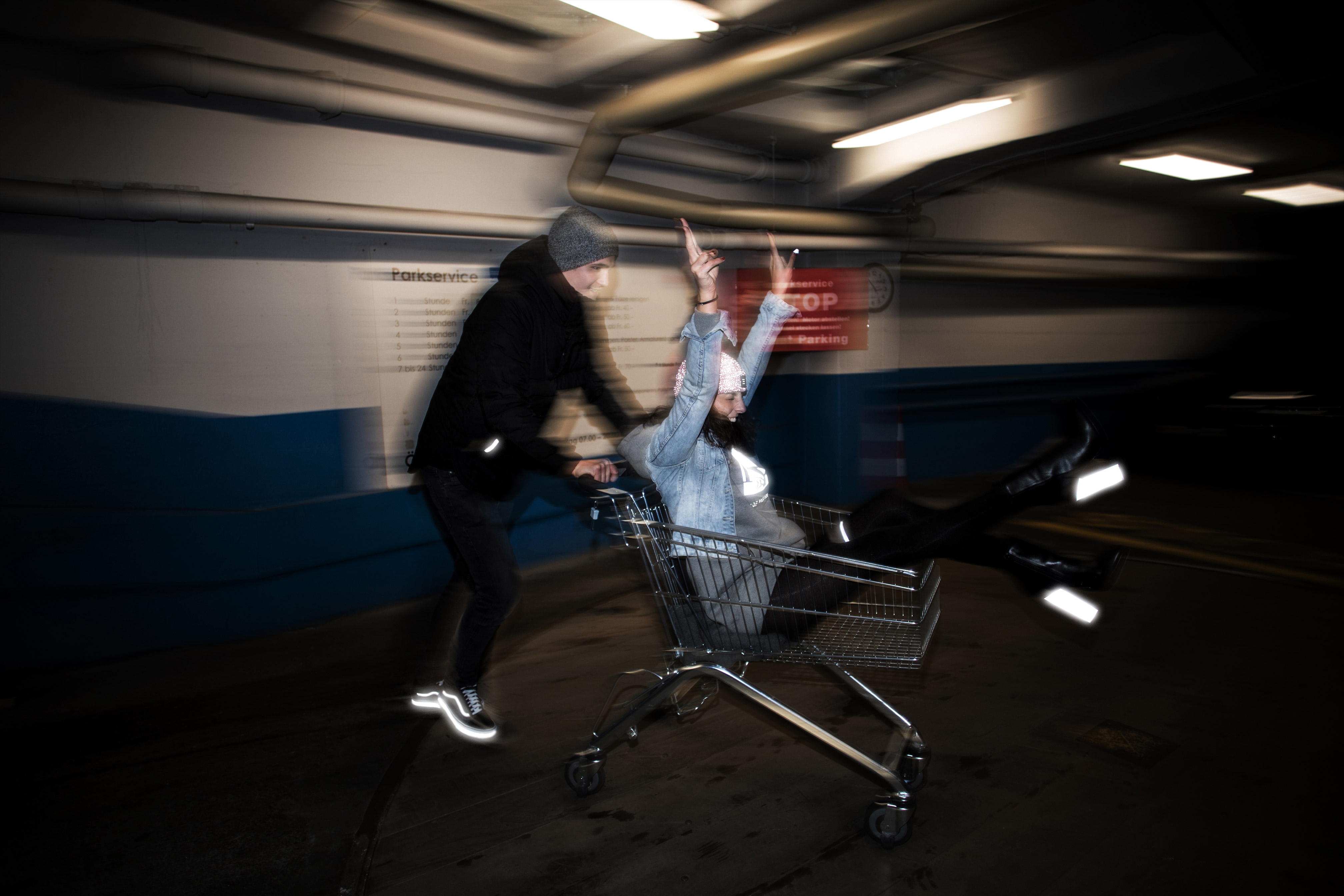 Kerl schiebt Mädchen im Einkaufswagen in einer Parkgarage reflektierende Stiefel und Vans