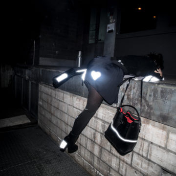 Mädchen in Dunkelheit über Wand klettert Herz auf schwarz Kleid schwarze Handtasche High Heels, reflective