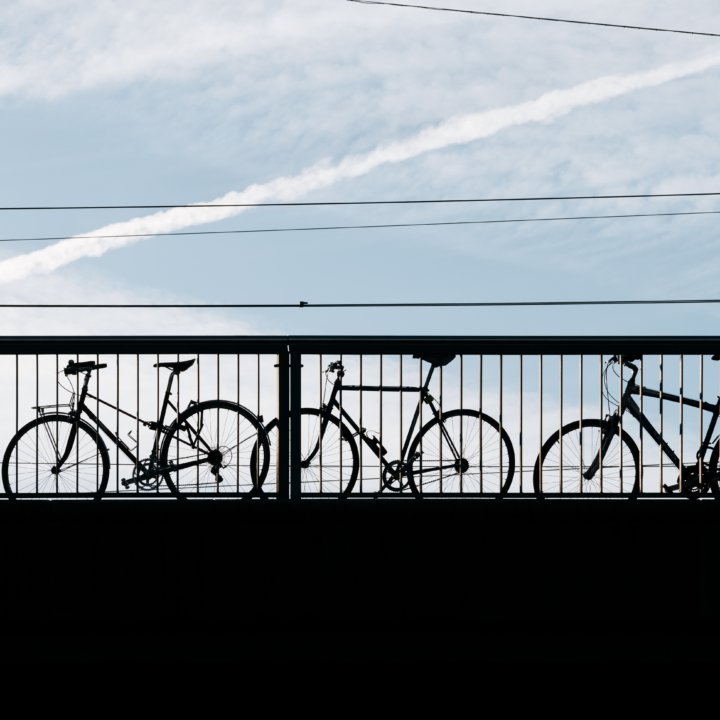 Silhouette eines Mannes mit einem Rucksack, der an drei Fahrrädern vorbeigeht, die an ein Brückengeländer gekettet sind.